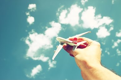 close up photo of man's hand holding toy airplane against blue sky with clouds. filtered image 