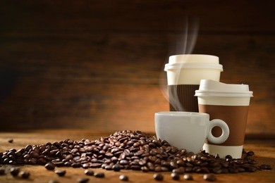 cups of coffee with smoke and coffee beans on old wooden background