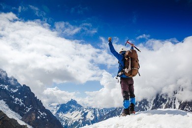 mountaineer reaches the top of a snowy mountain in a sunny winter day