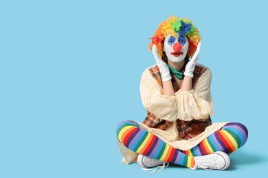 young woman dressed as sad clown sitting on blue background. april fool's day celebration