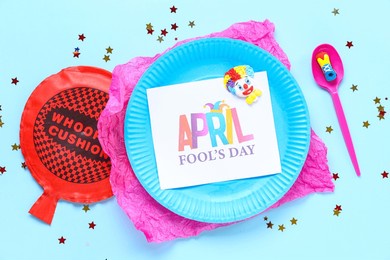 table setting with festive postcard, whoopee cushion and clown for april fools day on blue background