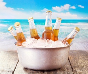 cold bottles of beer in bucket with ice over sea 
