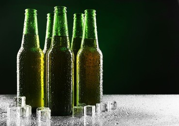 glass bottles of beer with ice cubes on dark background