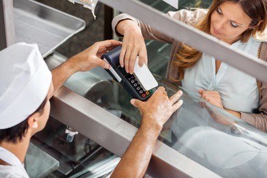 high angle view of mature female customer paying through smartphone at butchery