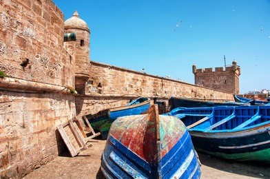 old rusty blue painted fishing boats in the port of essaouira, morocco with fortress walls and cannons