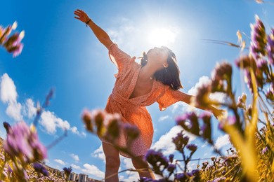 beautiful woman in a flower field raising her hands and enjoying the moment. summer mood. slender girl in a summer dress. girl on a background of flowers.