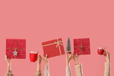 female hands with christmas gifts, cups of cocoa drink and decorative fir tree on pink background