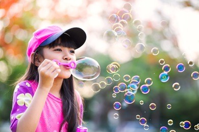 lovely little asian girl blowing soap bubbles, outdoor portrait