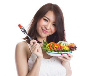 young woman eating a vegetable salad on white background
