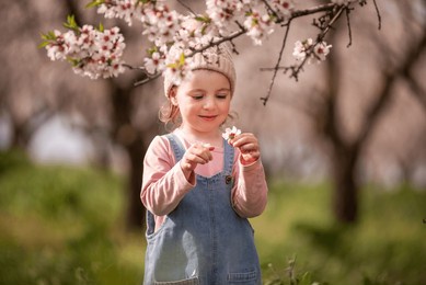 young child experiencing the joy of spring, holding a delicate flower with a happy expression, surrounded by blooming almond trees in a vibrant green field