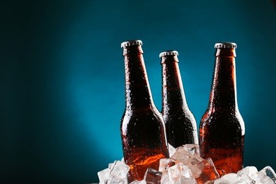 glass bottles of beer in ice cubes on color background