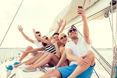vacation, travel, sea, friendship and people concept - smiling friends sitting on yacht deck and making selfie