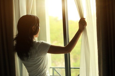 young woman opening curtains in a bedroom