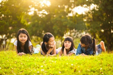 little asian girls laying on the green grass under sunlight