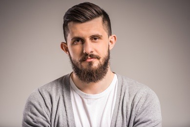 confident bearded man is looking at the camera, standing on gray background.
