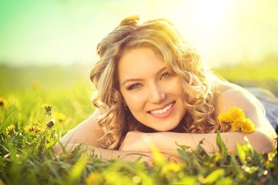 beautiful young woman lying on a field, green grass and dandelion flowers. outdoors enjoy nature. healthy smiling girl lying in green grass