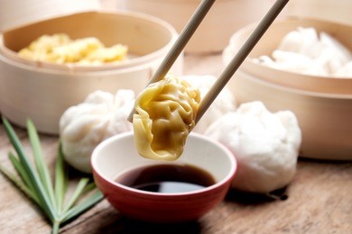 chinese steamed dumpling being dipped in soy sauce with chopsticks