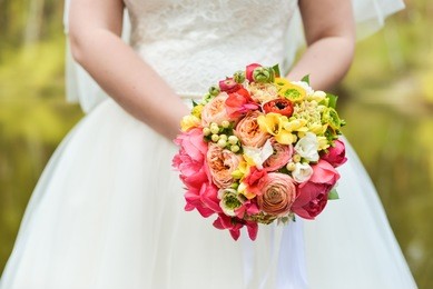 bride in white wedding dress holding a bouquet of bright flowers on green background