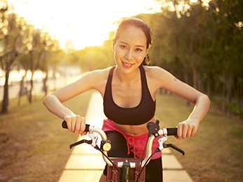 young and beautiful asian woman riding bicycle outdoors in park in warm sunlight, smiling and cheerful; fitness, sport and exercise, healthy life and lifestyle concept.