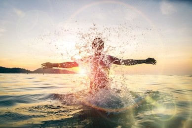 man splashing water during summer holidays - young attractive man having fun on a tropical beach at sunset