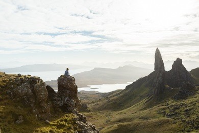 man sitting on huge rock after challenging climb to mountain summit in the isle of skye, scottish highlands, scotland.