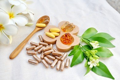 herbal supplements and vitamins  on wooden tray and wooden spoon, decorated with white flowers and green leafs background as white cotton cloth 