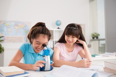 curious classmates looking into microscope: biology lesson