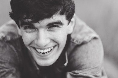 outdoor portrait of a manly  very beautiful sexy young man, dark hair, with a stunning smile, smiling and posing in the green grass in a white shirt and a denim jacket 
as the italian