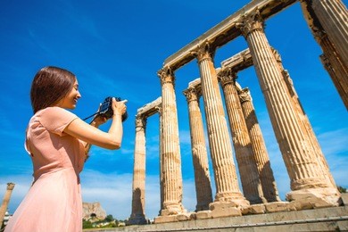 young and smiling woman photographer taking picture with professional camera of zeus temple in acropolis