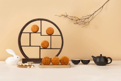 mid-autumn festival still life featuring mooncakes, traditional black wooden display shelf, ceramic teapot and cups, white rabbit figurine, and dried branches on beige background.