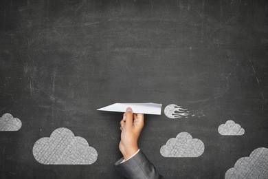 businessman hand holding paper plane on front of vintage full frame black blank blackboard no frame and couple clouds