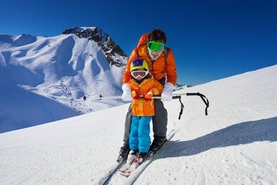 little boy learns to ski on mountain resort with instructor helping to learn how to turn with mountain on background