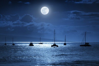 dramatic night time photo illustration of a deep midnight blue sky with, bright full moon, over calm ocean waves in maui, hawaii.   would make a great travel or vacation background.