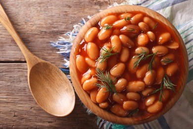 white beans in tomato sauce in a wooden bowl closeup. horizontal top view