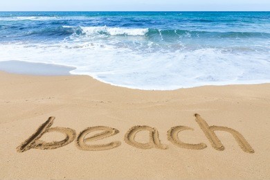 word beach on sandy coast with blue sea and water waves