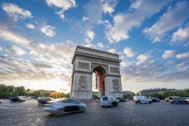 sunset with dramatic sky behind arc de triomphe and blurred cars traffic along the champs-elysees 