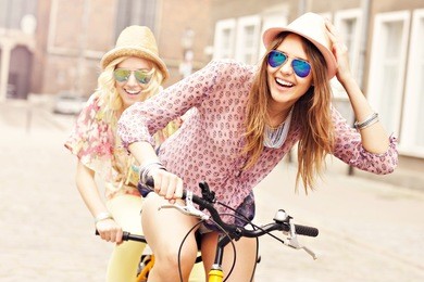a picture of two girl friends riding a tandem bicycle in the city