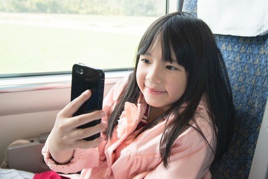 little asian girl smiling and sharing social media in a smart phone . she travels on a train