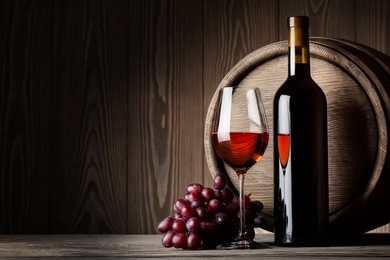 black bottle and glass of red wine with grapes and barrel on wooden background