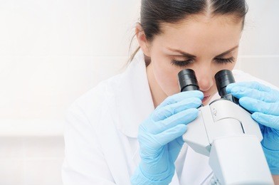 young woman medical researcher looking through microscope in laboratory, medicine concept