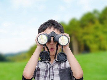 young asian boy using binoculars in forest