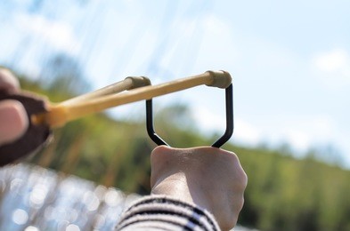 first person perspective of young boy holding sling shot, pulling rubber strips back in anticipation of catapult shot across lake