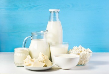 tasty healthy dairy products on a table on a blue background: sour cream in a white bowl, cottage cheese in bowl, cream in a a bank,  butter on a saucer and milk in a jar, glass bottle and in a glass
