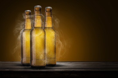 three bottles of beer with cold smoke over wooden table