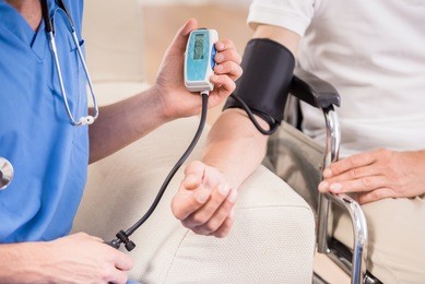 male doctor measuring blood pressure to older patient sitting at wheelchair.