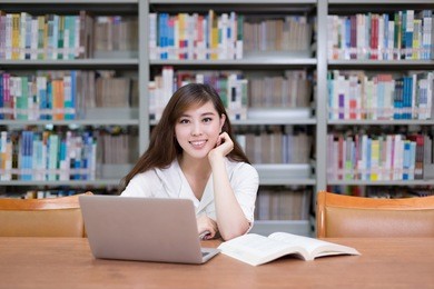 beautiful asian female student using laptop for study in library with bookshelf background.