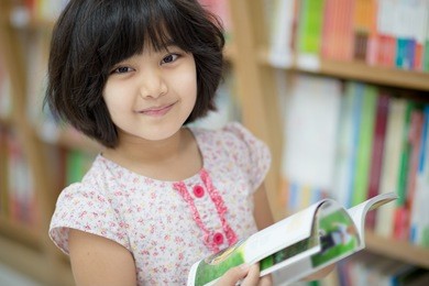little asian child reading a book on the library
