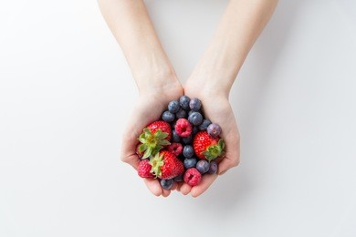 healthy eating, dieting, vegetarian food and people concept - close up of woman hands holding berries at home