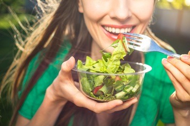 portrait of attractive caucasian smiling woman eating salad, focus on hand and fork. soft, backlight