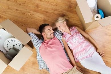 home, people, repair and real estate concept - happy couple with cardboard boxes and stuff lying on floor to new place